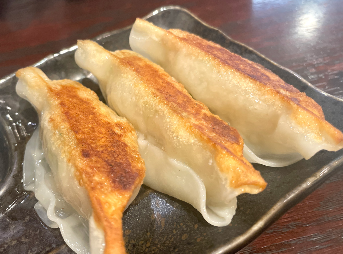 焦げ目のついた餃子3個が黒い皿に並んだアップ写真